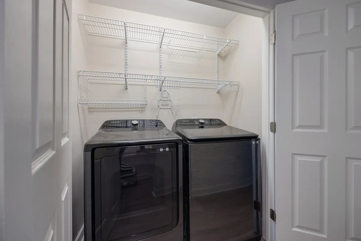 A tidy laundry room featuring a washer, dryer, and open shelving, organized for practical use and easy access to laundry essentials. The space is bright, functional, and designed to handle the everyday needs of families and longer-term guests.
