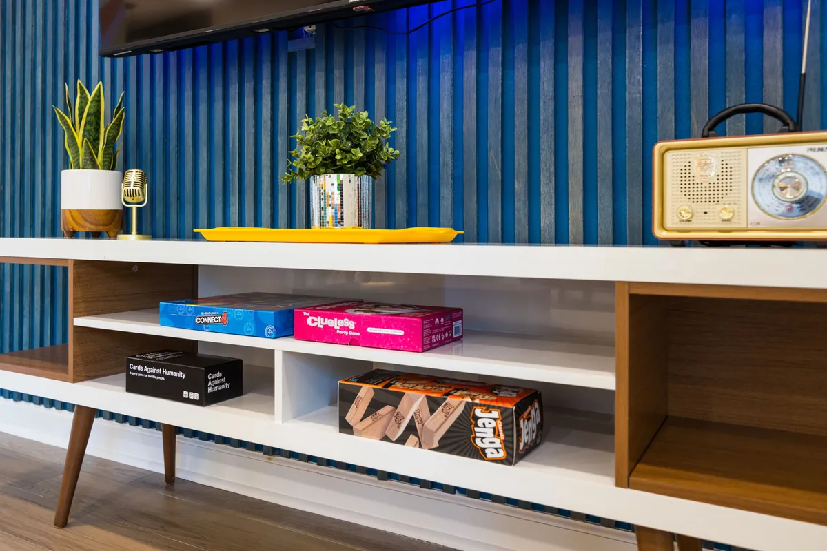 A cozy game nook with a collection of colorful board games, a retro radio, decorative plants, and a striped blue accent wall. The setup invites guests to unwind and share laughter during game nights or relaxed evenings.