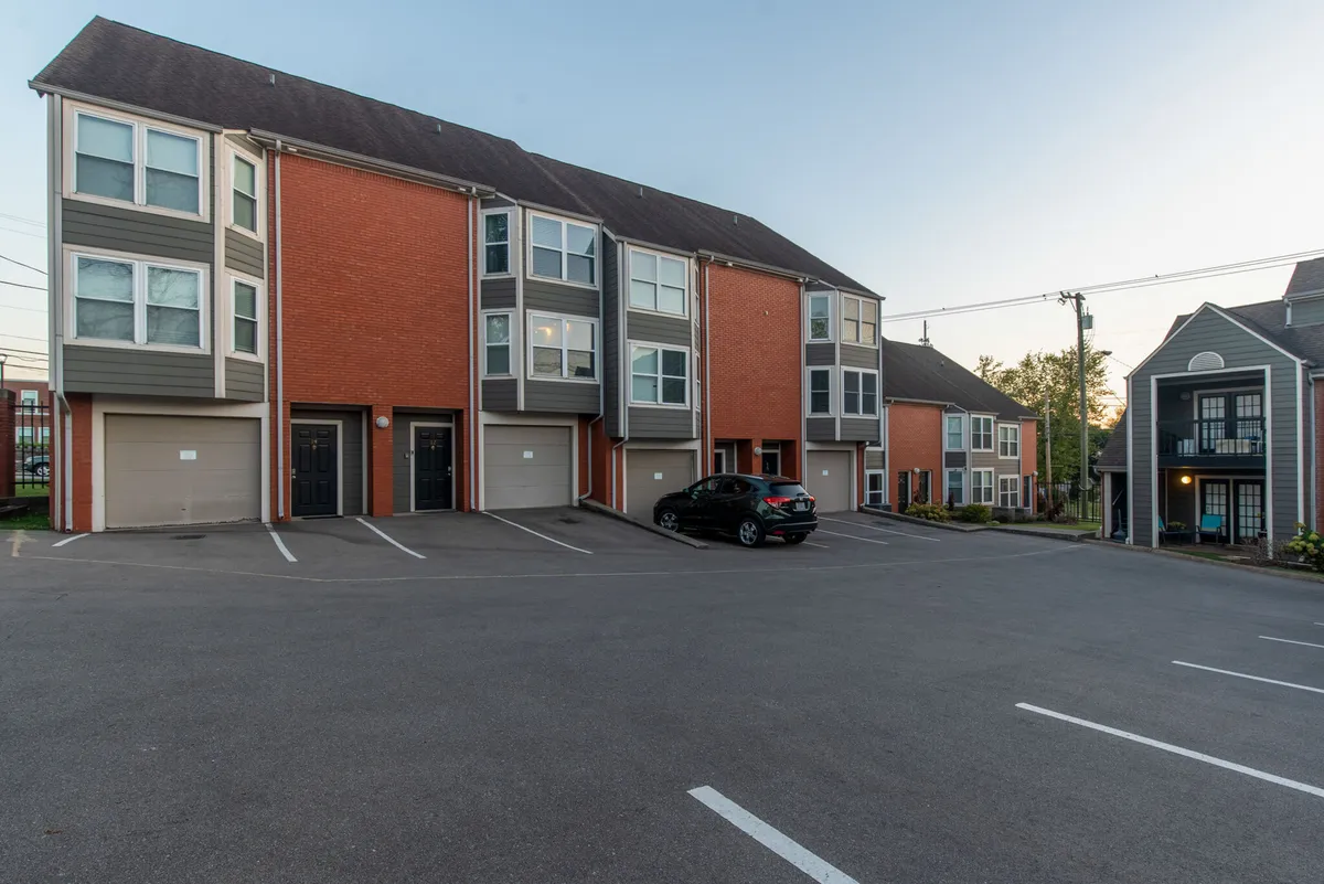 This exterior shot focuses on rows of modern townhouses with a dedicated parking area and landscaped surroundings, representing the secure, convenient housing option within the city. The mood is welcoming and practical.