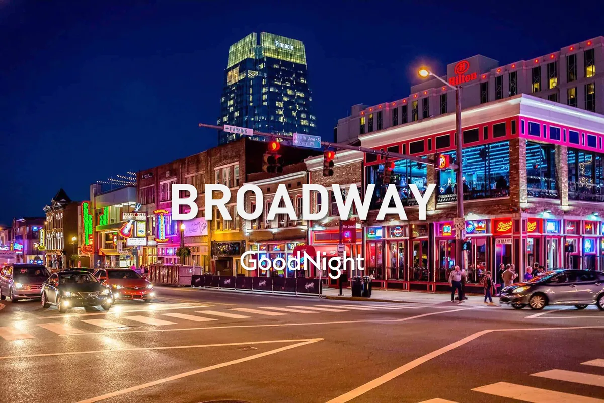 A lively exterior view of Broadway at night, with neon signs, bustling nightlife venues, cars, and pedestrians capturing the energetic spirit of downtown Nashville. The scene is vibrant with activity, highlighting the area's reputation for dining, live music, and festive gatherings.