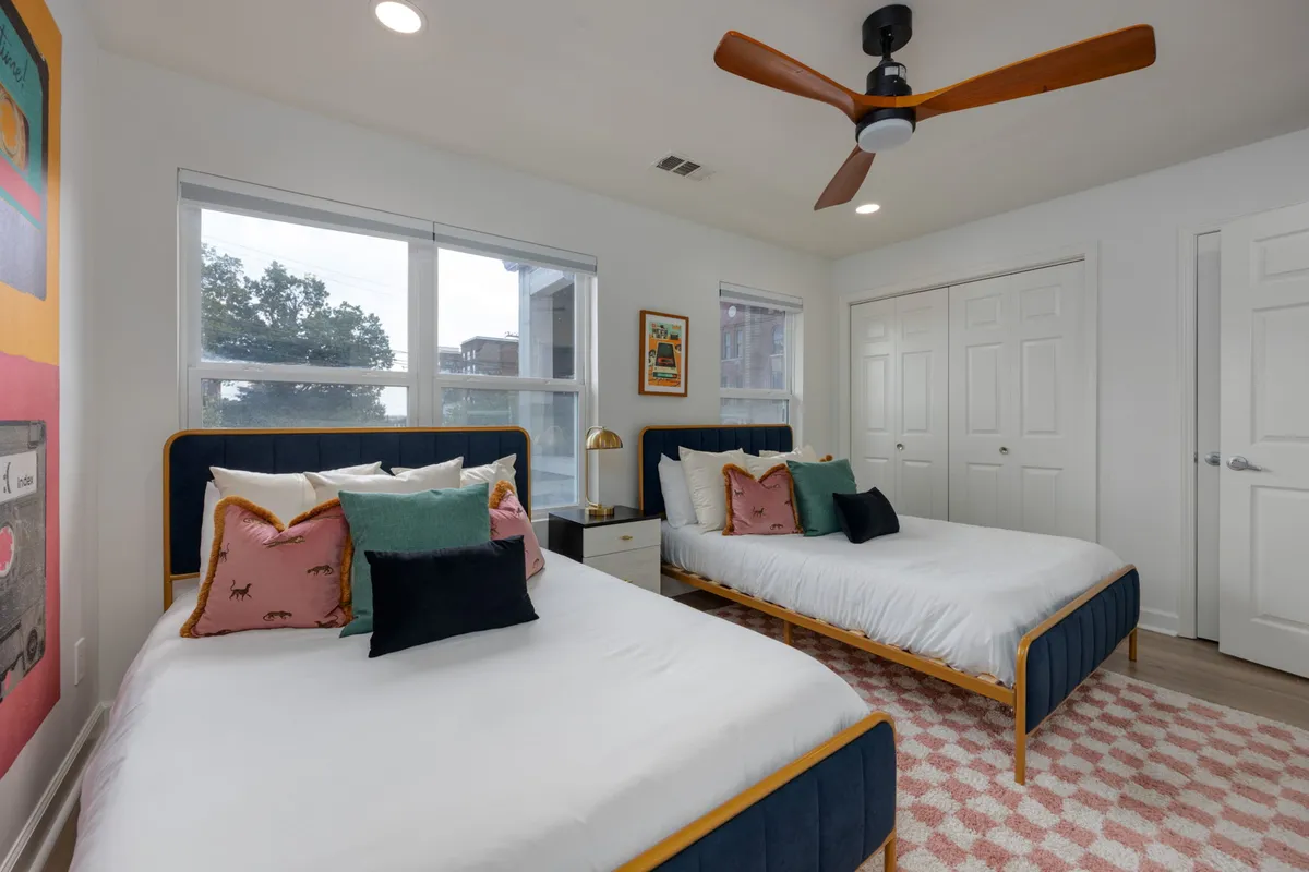 A cozy bedroom with two beds adorned with colorful pillows, wall art above the headboards, and a nightstand with a lamp between them, creating a welcoming and flexible sleeping environment for guests or families.