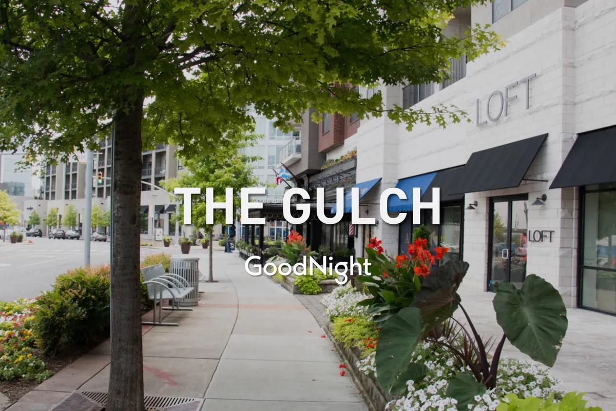 The scene features tree-lined walkways, colorful flowers, charming storefronts, and benches—inviting spaces for couples to stroll, shop, and enjoy lively neighborhood vibes.