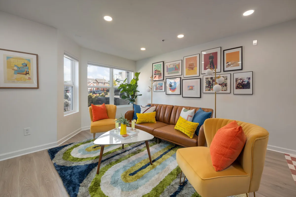 A cheerful and inviting living area with a leather sofa, vibrant accent chairs, bold artwork, a coffee table with decorative objects, and a woven area rug, providing a versatile space for families or friends to gather, relax, and socialize.